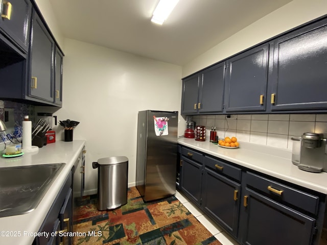 kitchen featuring freestanding refrigerator, light countertops, a sink, and backsplash