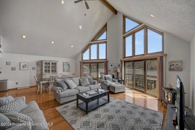 living room featuring beamed ceiling, wood-type flooring, high vaulted ceiling, and a wood stove