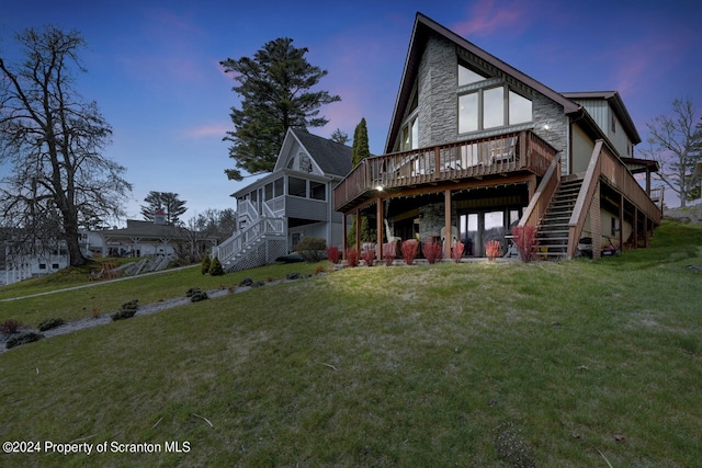 back house at dusk with a sunroom, a deck, and a yard