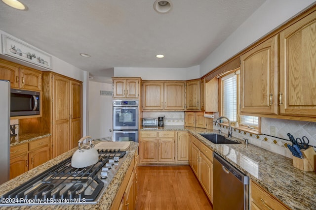 kitchen with light stone countertops, sink, light hardwood / wood-style flooring, decorative backsplash, and appliances with stainless steel finishes