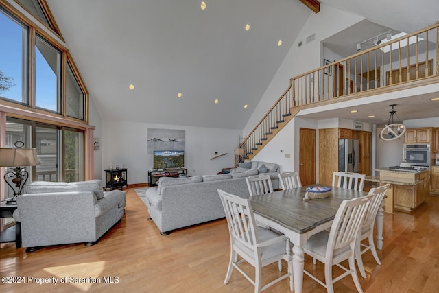 dining room featuring light hardwood / wood-style floors, a wood stove, beam ceiling, and high vaulted ceiling