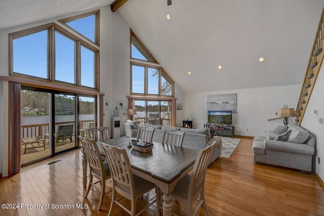 dining space featuring beam ceiling, a water view, high vaulted ceiling, and light hardwood / wood-style floors