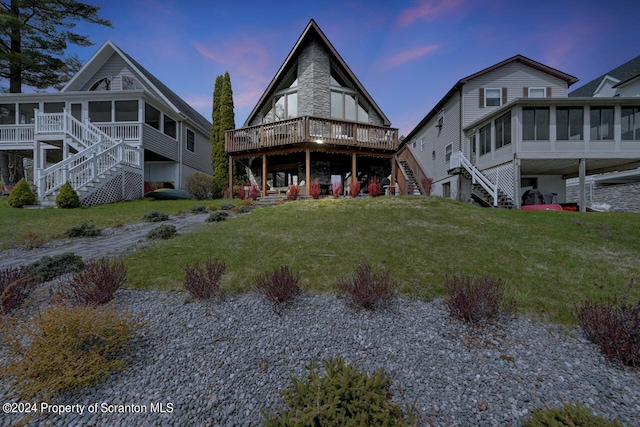 back house at dusk featuring a wooden deck, a sunroom, and a yard