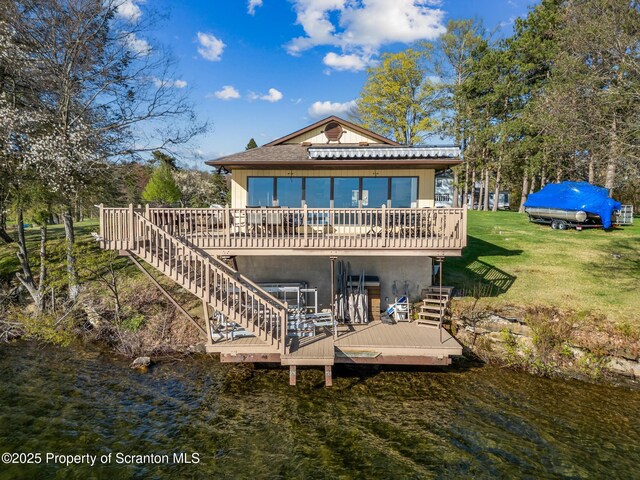 rear view of property with stairway, a deck with water view, and a lawn