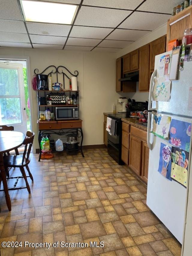 kitchen with black range with electric cooktop, a drop ceiling, and white refrigerator