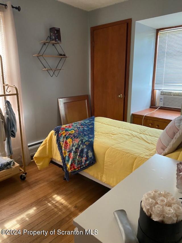 bedroom with baseboard heating, a closet, cooling unit, and hardwood / wood-style flooring