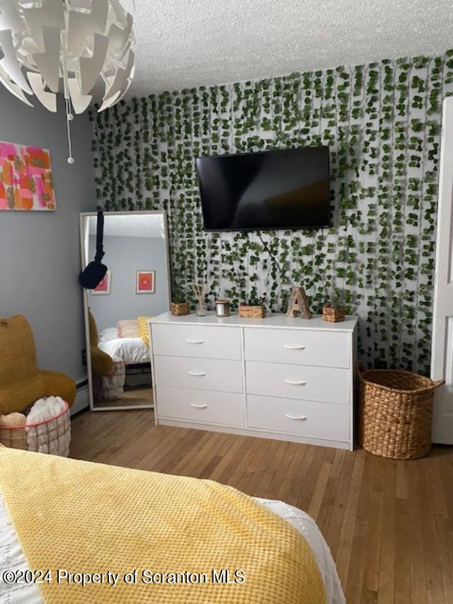 bedroom with hardwood / wood-style floors, a baseboard radiator, a textured ceiling, and an inviting chandelier