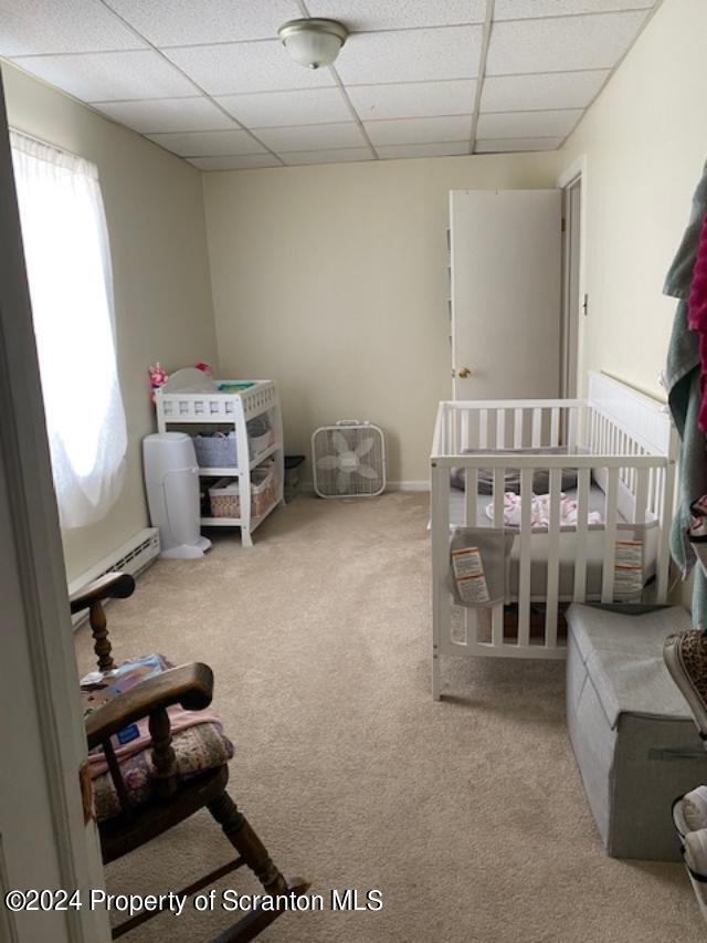 bedroom with a paneled ceiling, a baseboard radiator, light colored carpet, and a crib