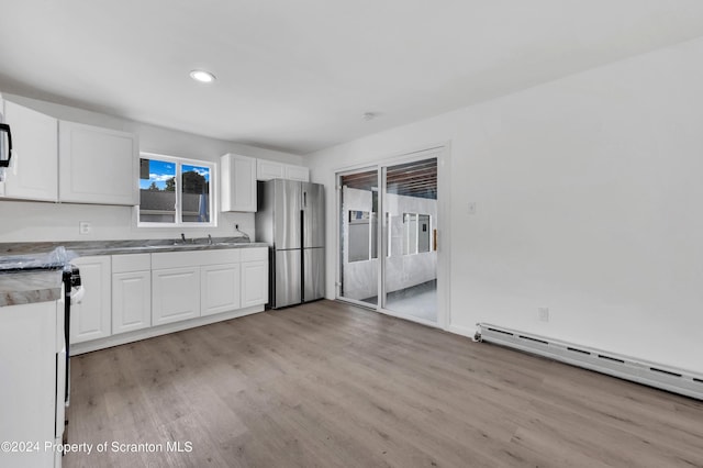 kitchen with stainless steel refrigerator, sink, a baseboard heating unit, light hardwood / wood-style floors, and white cabinets