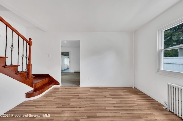 unfurnished room featuring light wood-type flooring, baseboard heating, plenty of natural light, and radiator