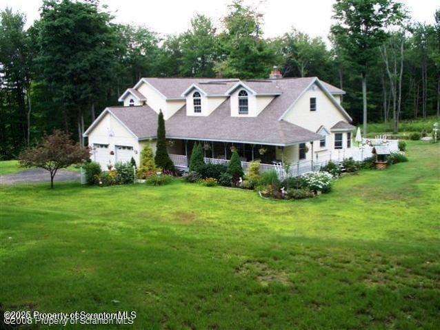 new england style home with covered porch, a front lawn, and an attached garage