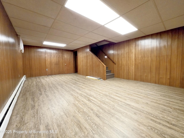 finished basement featuring a baseboard heating unit, a paneled ceiling, wooden walls, and wood finished floors