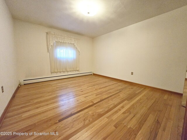 unfurnished room featuring wood finished floors, a baseboard heating unit, and baseboards