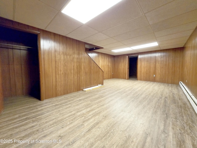 finished basement featuring baseboard heating, wood walls, wood finished floors, and stairs