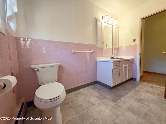 bathroom with tile walls, vanity, toilet, a wainscoted wall, and baseboard heating