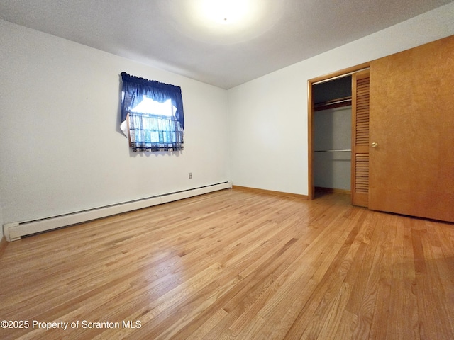 unfurnished bedroom featuring a baseboard heating unit, light wood finished floors, and a closet