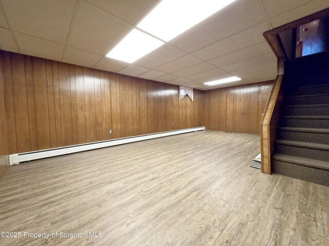 finished basement featuring baseboard heating, wood finished floors, wooden walls, and a drop ceiling