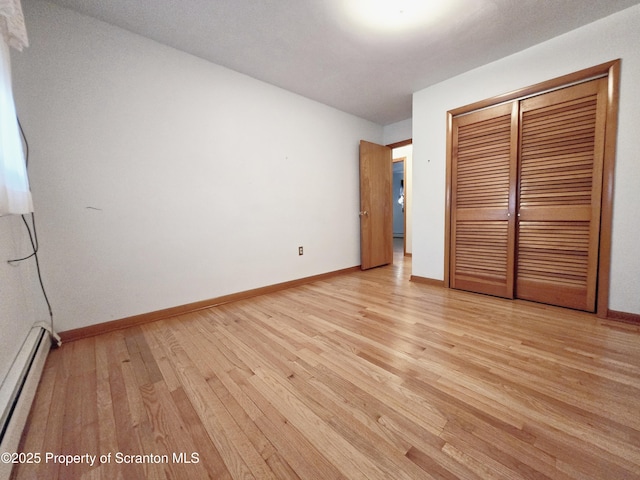 unfurnished bedroom featuring a baseboard heating unit, a closet, light wood-style flooring, and baseboards