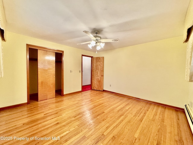 unfurnished bedroom featuring a closet, light wood-style flooring, a baseboard heating unit, a ceiling fan, and baseboards