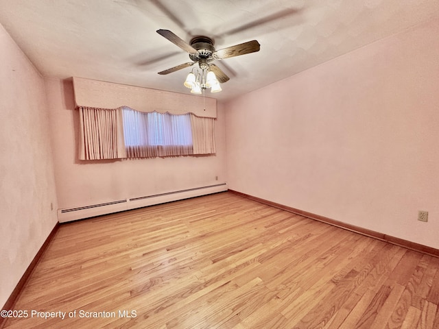 spare room featuring a baseboard radiator, baseboards, and wood finished floors