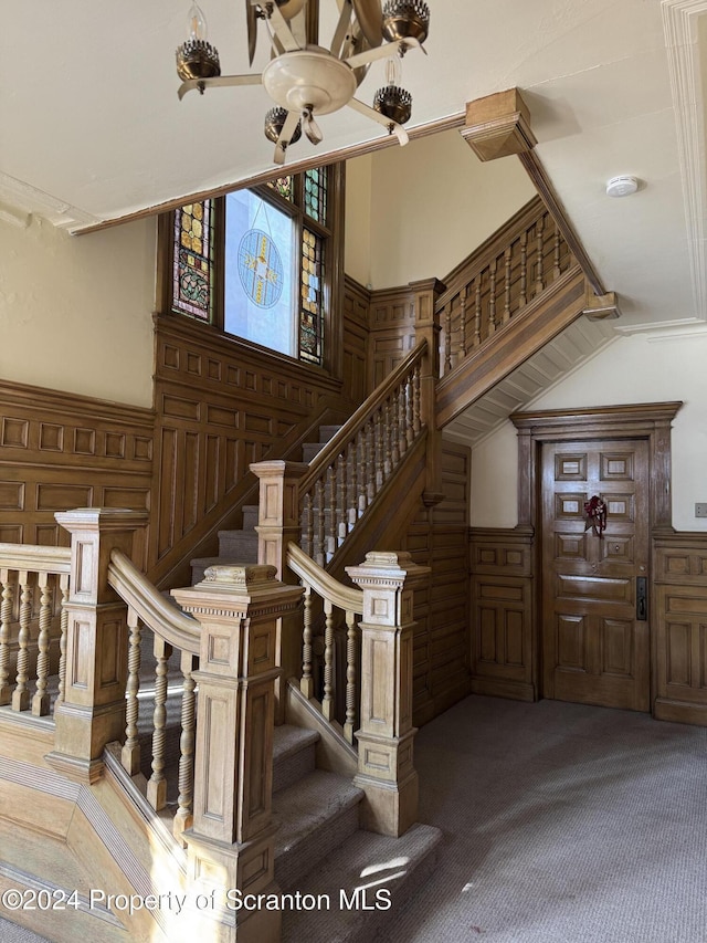 staircase with a towering ceiling, carpet floors, and wooden walls