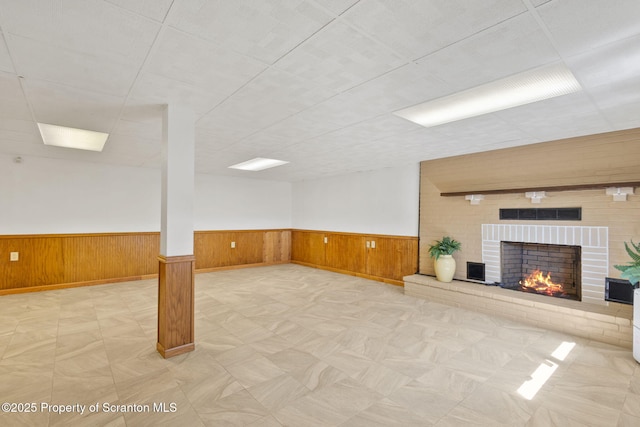 basement with wainscoting, a brick fireplace, and wood walls