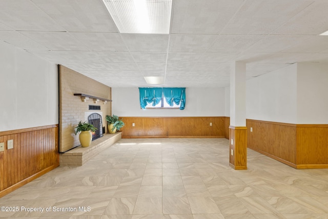 below grade area featuring a wainscoted wall, wood walls, and a brick fireplace