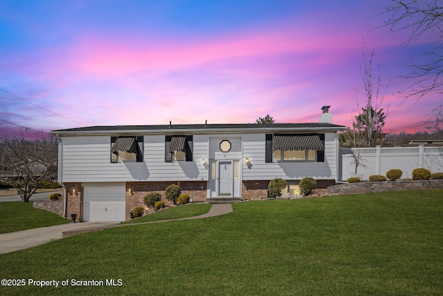 split foyer home featuring a yard, concrete driveway, a chimney, and fence