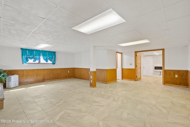 below grade area featuring a drop ceiling, a wainscoted wall, heating unit, and wooden walls