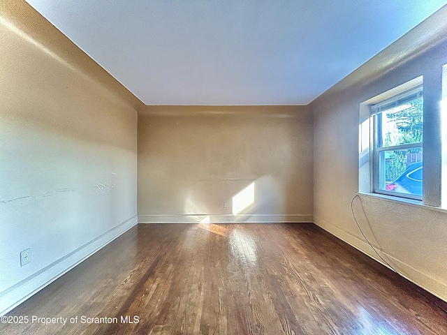 spare room with baseboards and wood finished floors