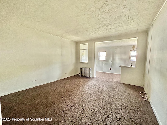 empty room with radiator heating unit, baseboards, and dark colored carpet