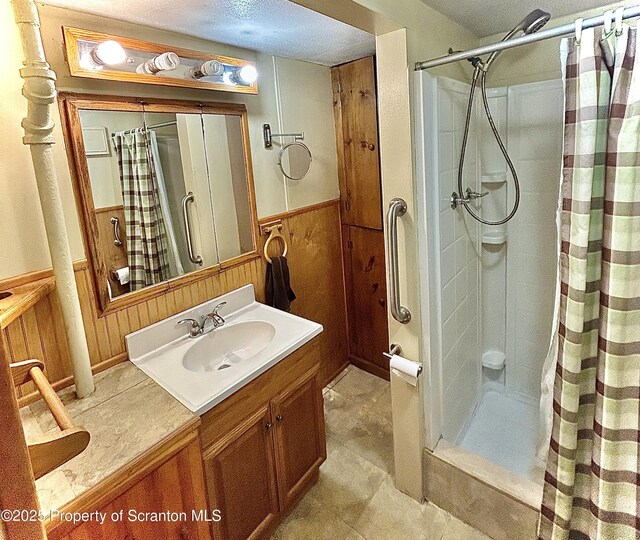 full bathroom featuring vanity, wood walls, wainscoting, and a shower stall
