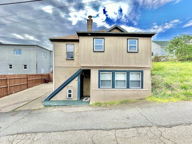 view of front of house with fence, a chimney, and stucco siding