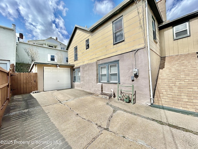 back of house featuring fence, an outdoor structure, an attached garage, and driveway