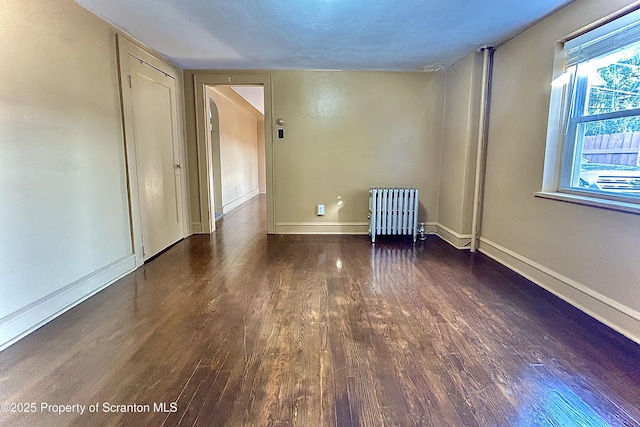unfurnished room with wood finished floors, baseboards, and radiator heating unit