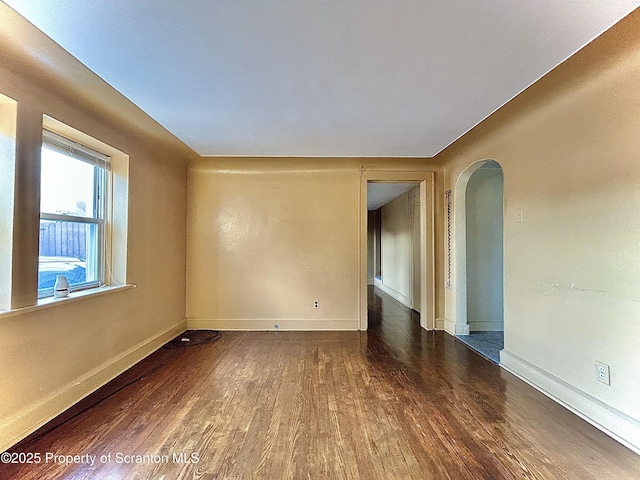 unfurnished room featuring baseboards, arched walkways, and wood finished floors