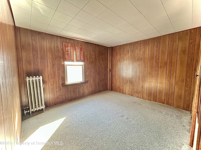 unfurnished room featuring radiator heating unit, carpet flooring, and wood walls