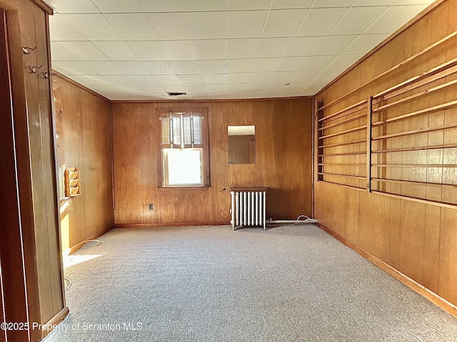 carpeted spare room featuring wood walls and radiator