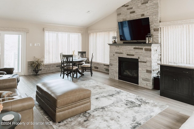 living room featuring a stone fireplace, plenty of natural light, light hardwood / wood-style floors, and lofted ceiling