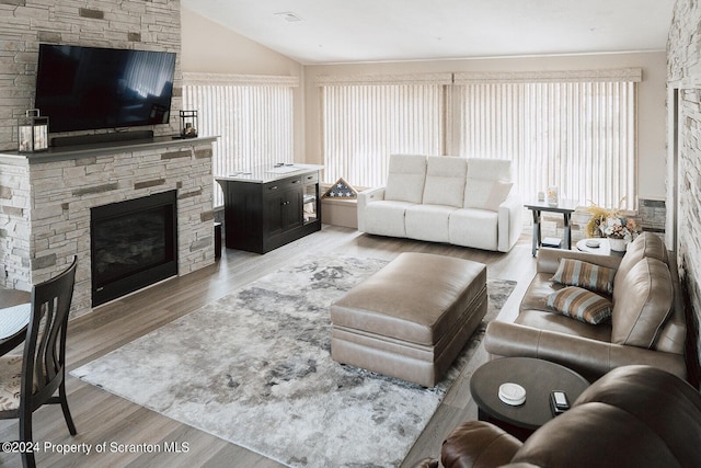 living room with hardwood / wood-style floors, a stone fireplace, and lofted ceiling