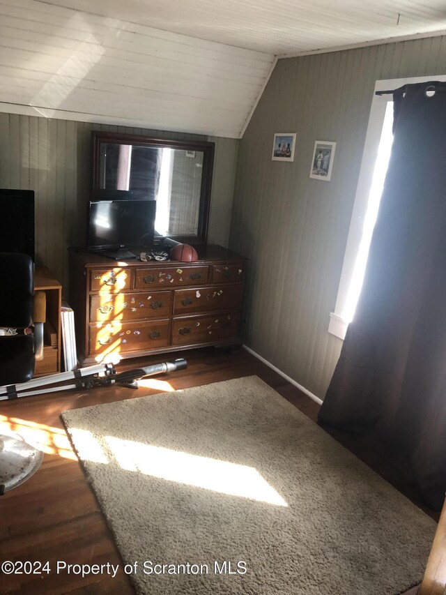 bedroom with dark hardwood / wood-style flooring, lofted ceiling, and wood walls