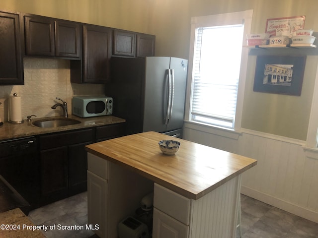 kitchen with wood counters, a wealth of natural light, dark brown cabinets, sink, and black dishwasher