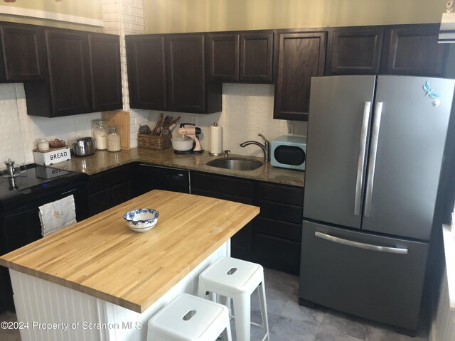 kitchen with a kitchen breakfast bar, stainless steel refrigerator, sink, and backsplash