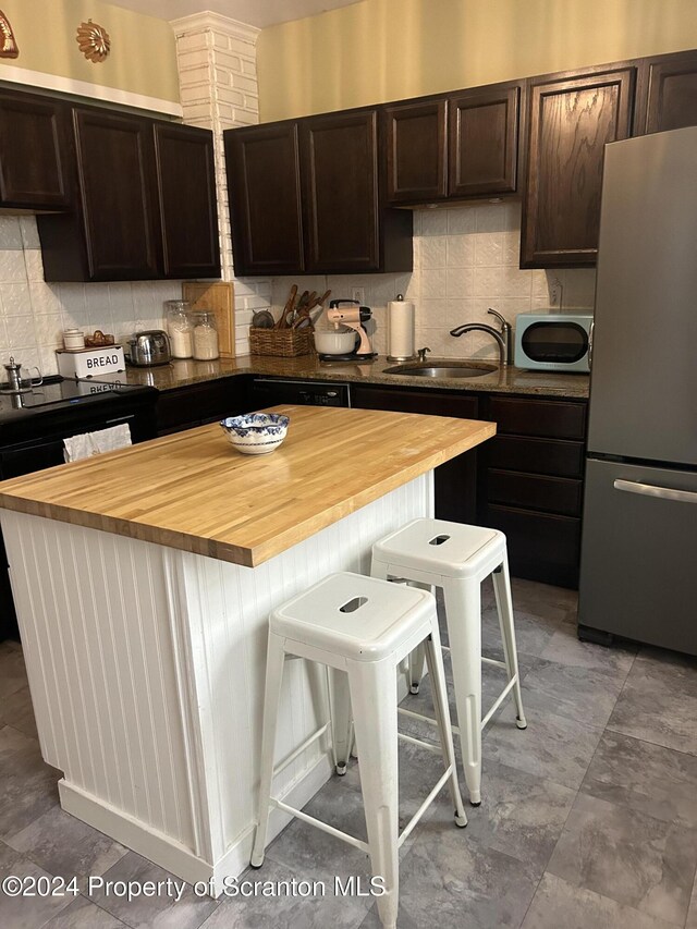 kitchen featuring stainless steel refrigerator, sink, wooden counters, a kitchen bar, and a kitchen island