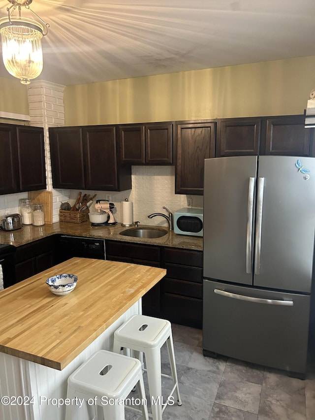 kitchen featuring wooden counters, a kitchen bar, tasteful backsplash, sink, and stainless steel refrigerator