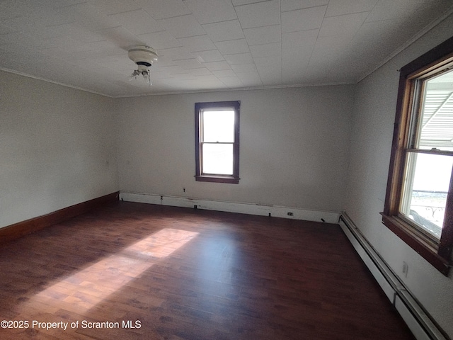 spare room with baseboard heating, plenty of natural light, wood finished floors, and crown molding