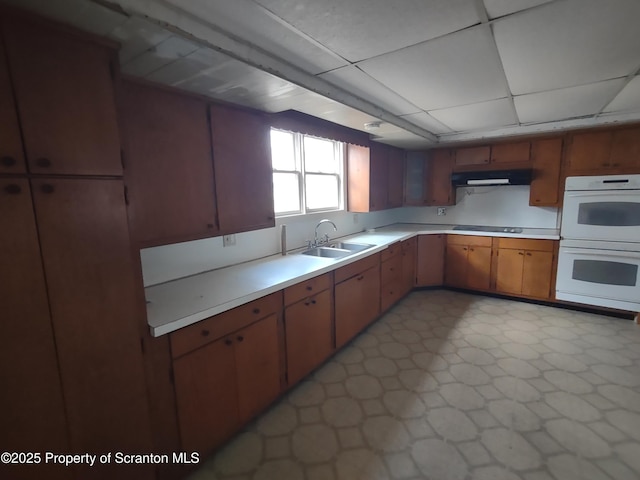 kitchen featuring double oven, under cabinet range hood, a sink, light countertops, and light floors