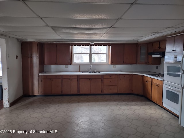 kitchen with under cabinet range hood, light countertops, a sink, and white double oven