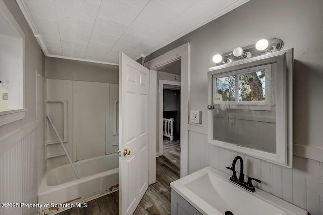 bathroom featuring a wainscoted wall, tub / shower combination, wood finished floors, and vanity