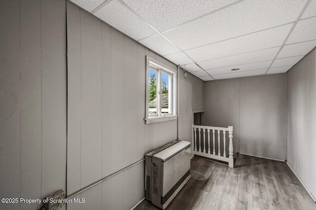 basement featuring a drop ceiling, heating unit, and wood finished floors